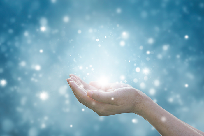 two hands cupped with tiny bright snow flakes all around, on a blue background
